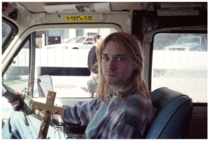 Kurt Cobain in the passenger seat of a van, looking directly into the camera.